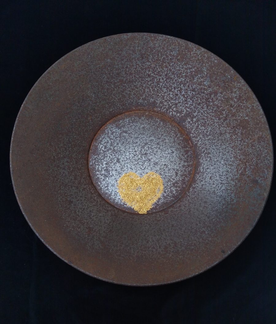 Fine gold flakes arranged in the shape of a heart in the centre of a dark gold pan.