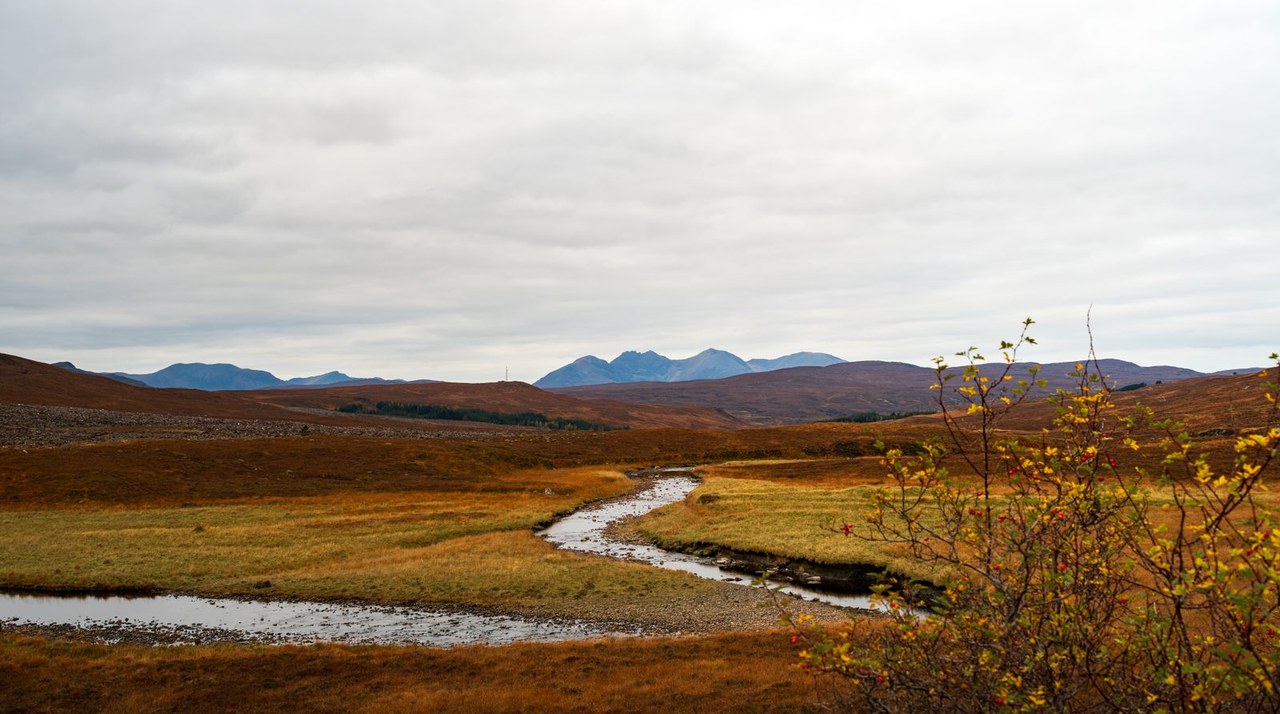 Peat-brown heather moorland and a winding upland river under an overcast sky — the kind of Dalradian country that drains a gold belt.