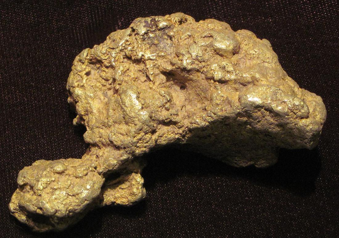 A natural placer gold nugget with a deep buttery-yellow colour and a soft, rounded, dimpled surface on a dark background.