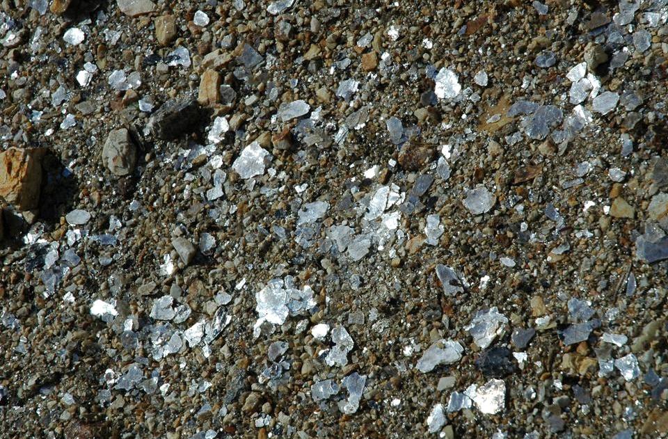 Sheets of silvery muscovite mica and dark biotite mica in granite, splitting into thin reflective flakes.