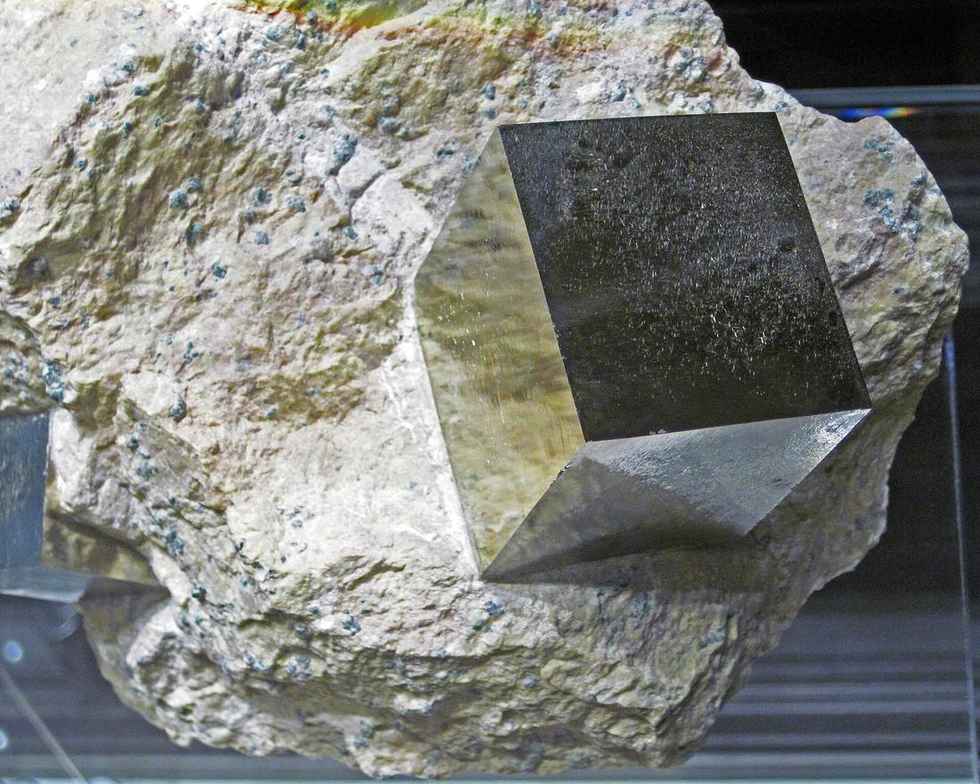 A sharp, perfectly cubic brassy-yellow pyrite crystal embedded in pale grey rock — the classic fool's gold cube.